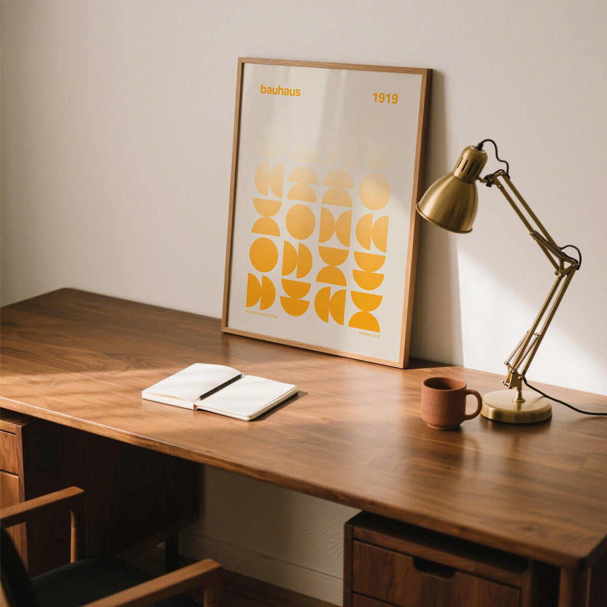 Posters Bauhaus leaning on a wood desk with a gold desk lamp and a notebook