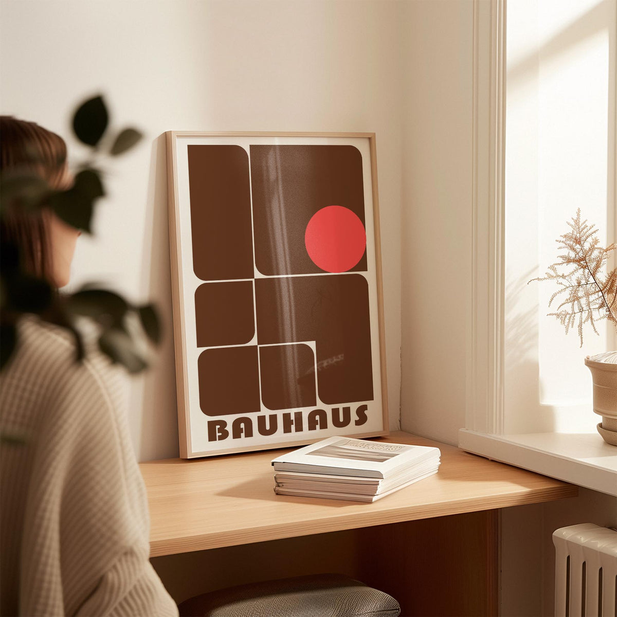 Wall Art for Offices leaning print with brown geometric shapes and red circle on a wooden desk with books and plant