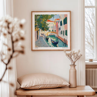 Venice wall art of gondolas and canal in warm colours framed above a table with a beige cushion and vase