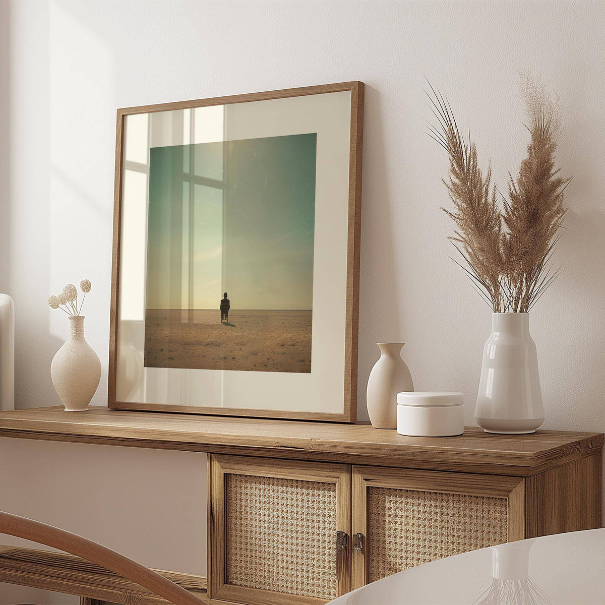 Framed Minimalist Surrealism Art of a person sitting in a desert with soft blue and beige tones on a sideboard