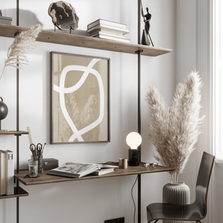 Minimalist art wall print with curved white lines in neutral tones above a wooden desk with a lamp and pampas grass