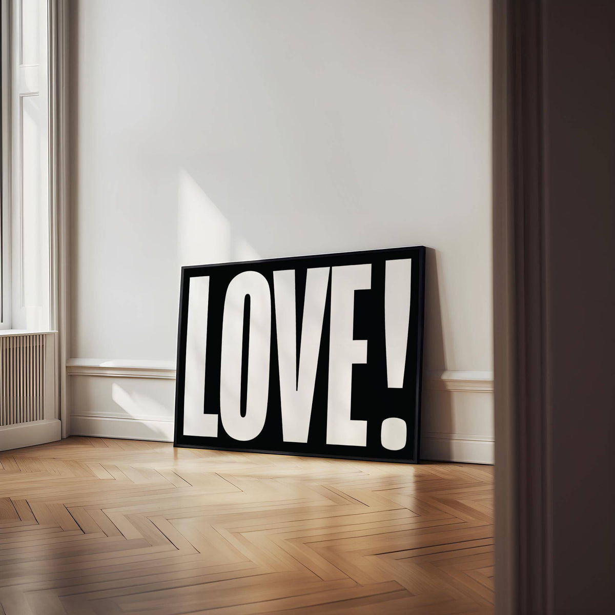 Print leaning on floor with LOVE typography in white on black in a room with wooden floor