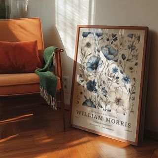 Neutral wall art leaning on floor showing blue and ivory botanical flowers next to an orange sofa