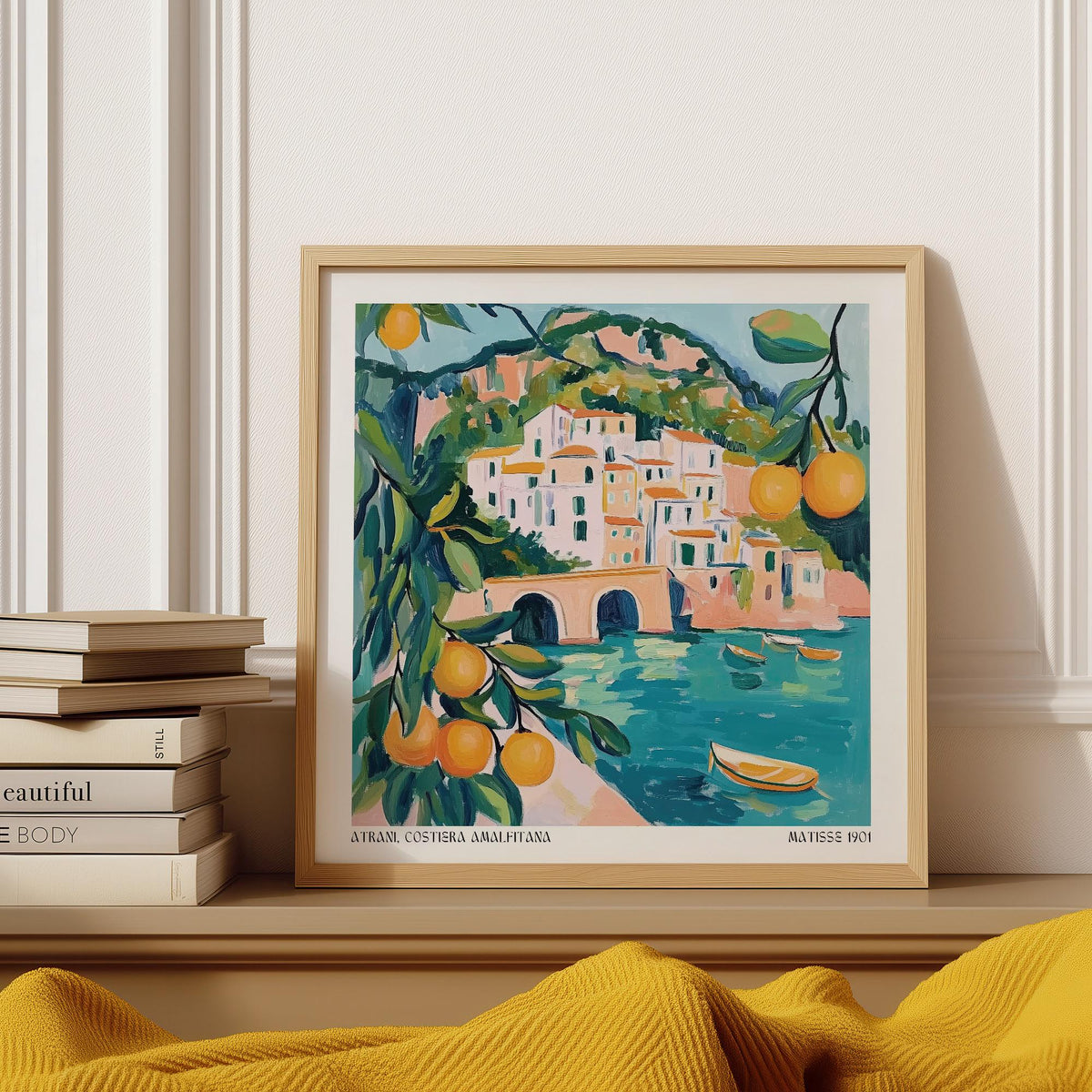 Framed Amalfi Coast painting of coastal town with citrus in blue and orange tones on a shelf with books