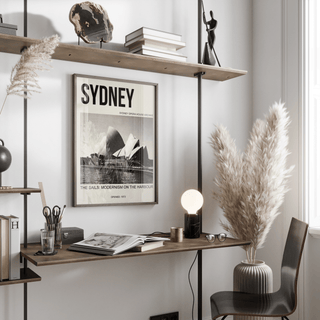 Sydney Opera House Poster framed print on wall above a wooden desk with books and a lamp