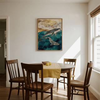 Whale art print of two whales in blue and gold tones above a dining table with wooden chairs