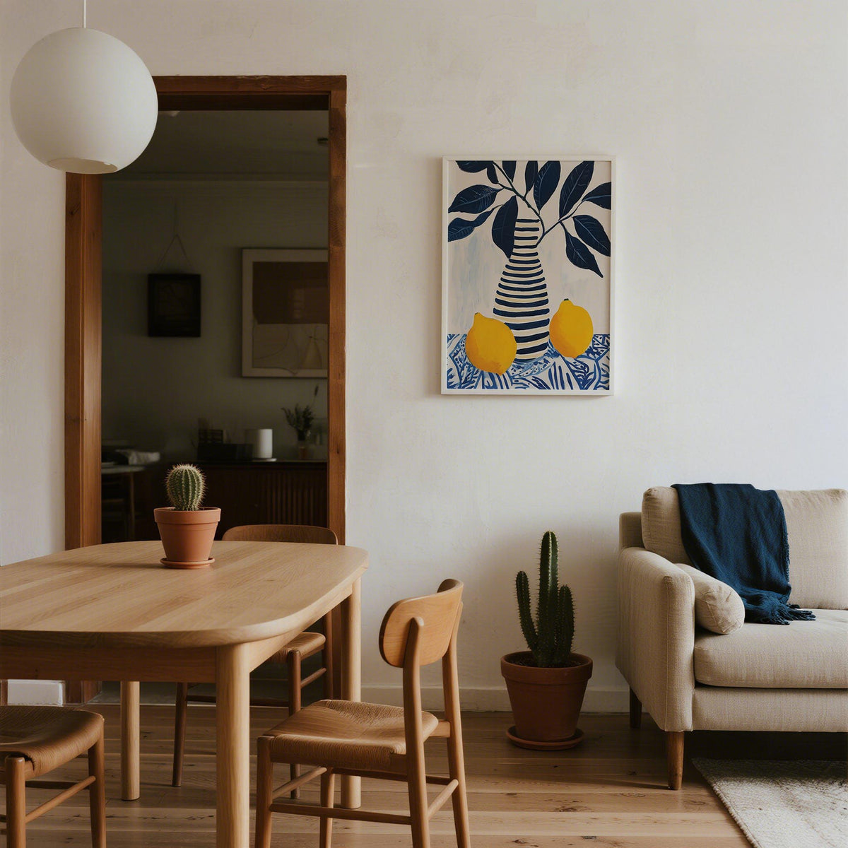 Print on a wall of striped vase with lemons and leaves in blue and yellow above a cactus in a modern living room