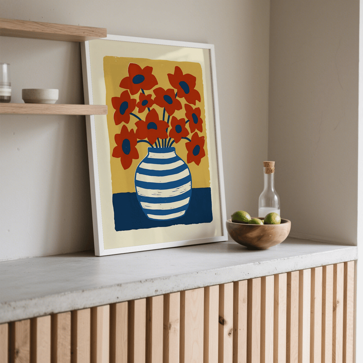 Print leaning on a shelf with a striped vase and red flowers next to a wooden bowl and glass bottle