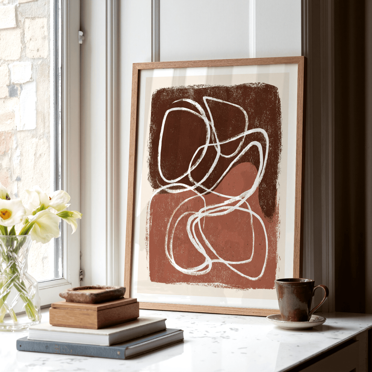 Minimalist Shapes wall art with brown and terracotta abstract shapes leaning on a table by a window with flowers