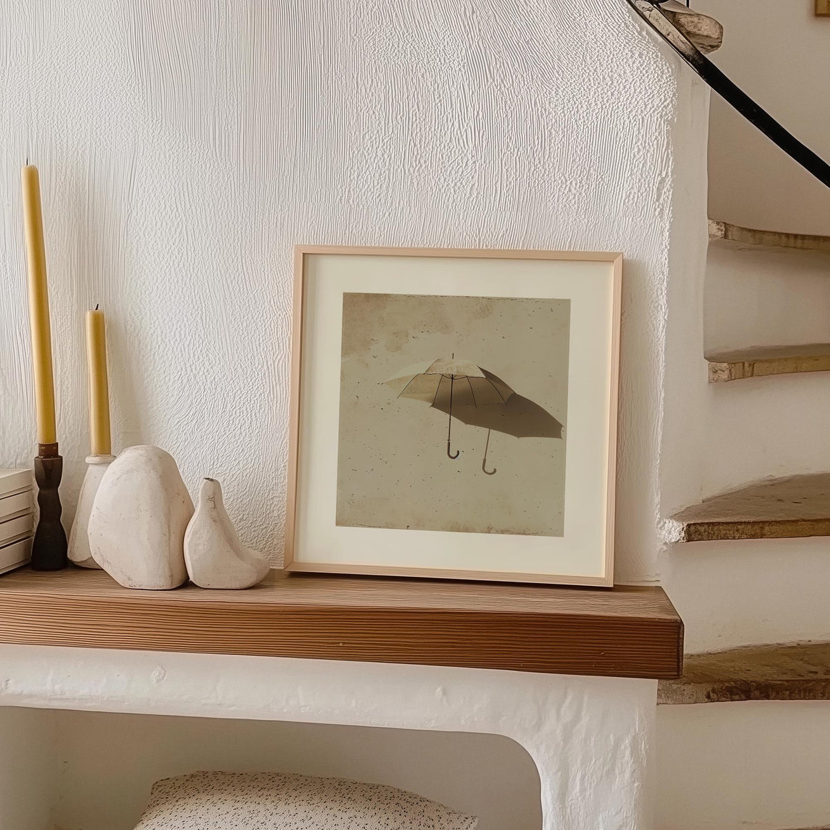 Surrealism Prints leaning on a shelf with ceramic vases and candles beside a staircase