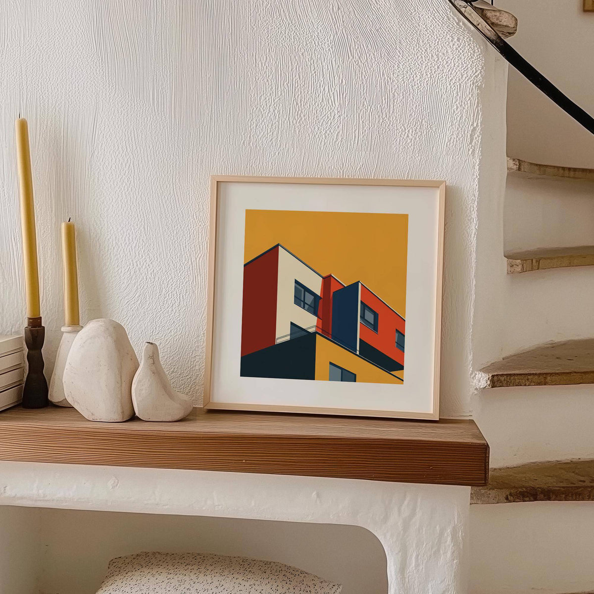 Print leaning on a shelf showing a modern abstract building in red yellow and blue next to candles and pottery