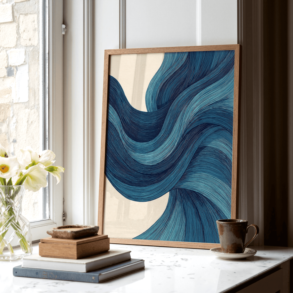 Print leaning on a shelf of blue wave lines in an abstract minimalist style with a cup and books nearby