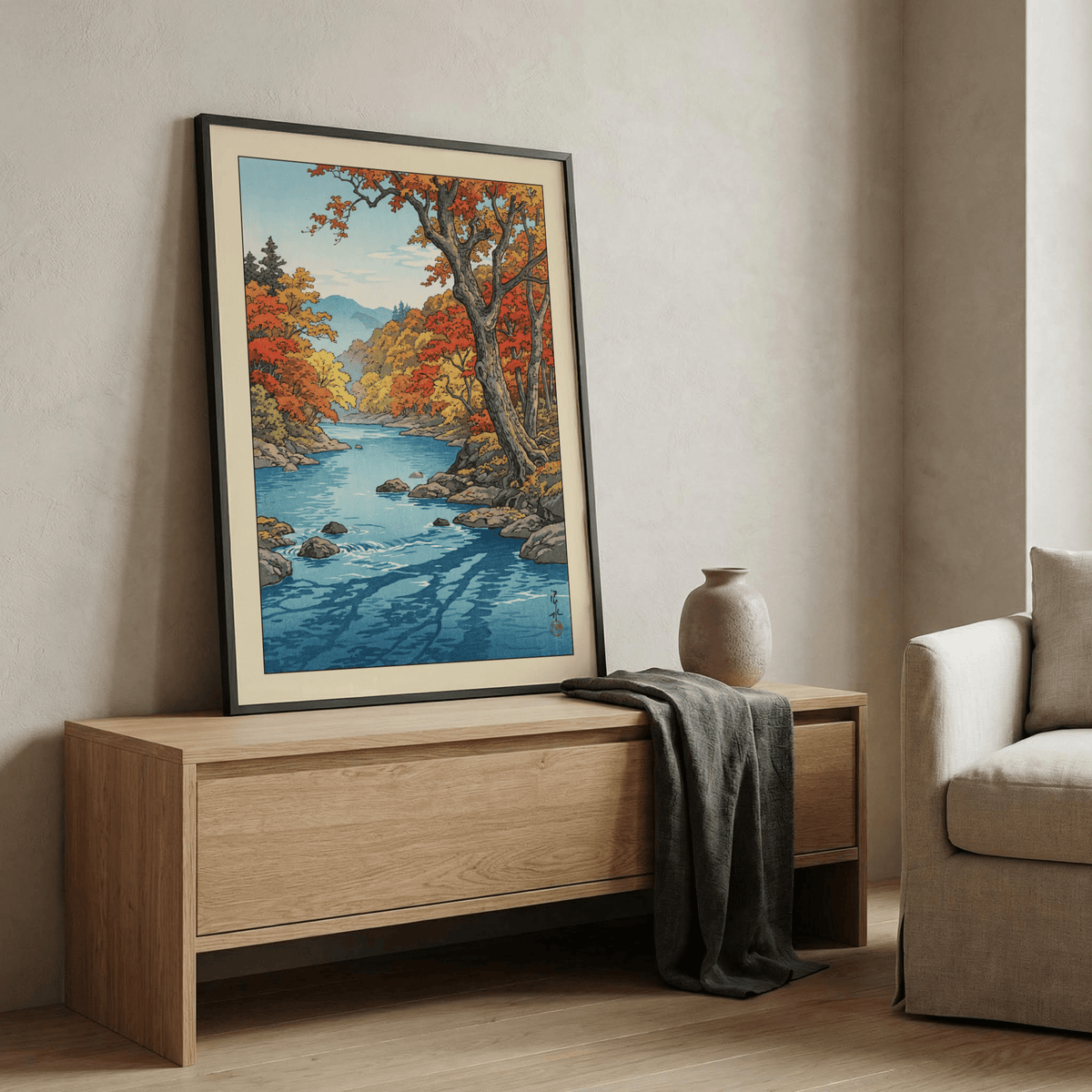 Print leaning on a shelf of Hasui Kawase Autumn Print with orange and yellow leaves and blue river with a vase nearby