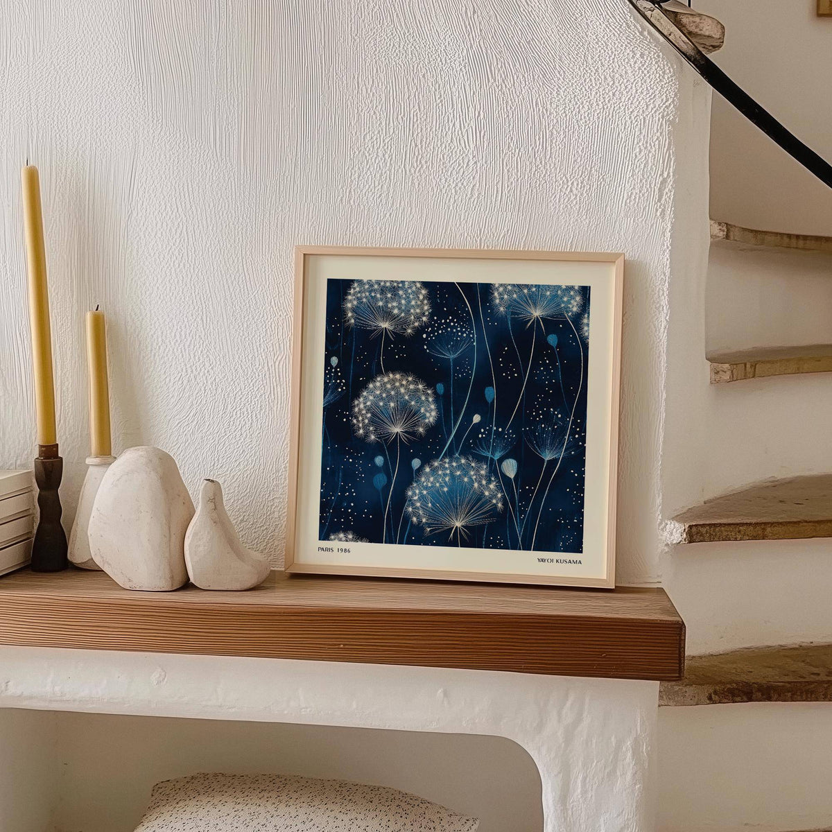 Print leaning on a shelf with blue dandelion seed heads and minimalist style with ceramic objects