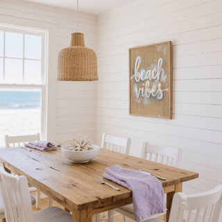 Beach Vibes wall art with white text on beige background above wooden dining table with bowl and purple linen in a white room