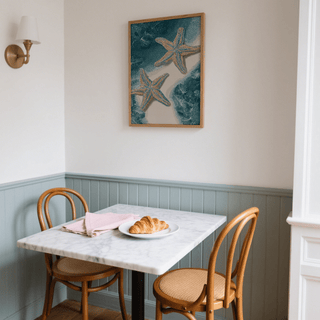 Underwater Starfish Print hanging above a dining table with a croissant and pink napkins