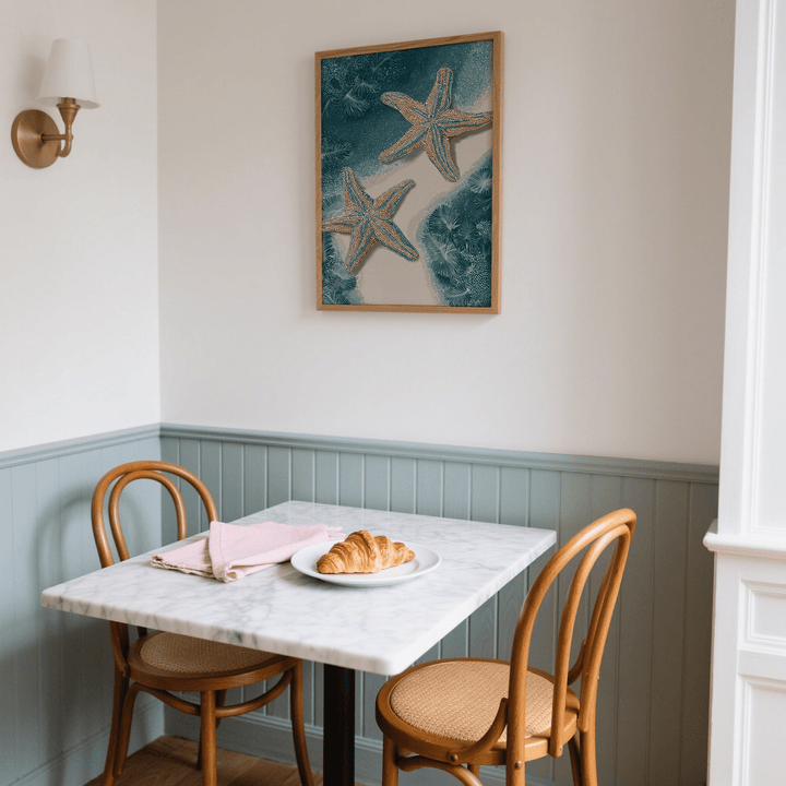 Underwater Starfish Print hanging above a dining table with a croissant and pink napkins