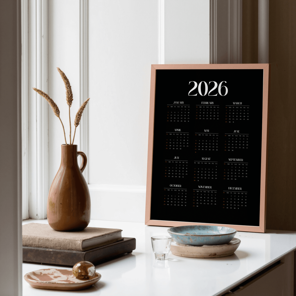 Framed Modern Calendar Print with 2026 calendar in black and white standing on a white surface with pottery and books