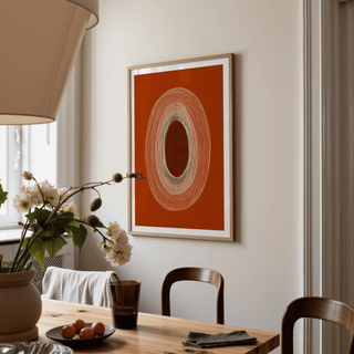 Abstract Line Drawing Poster on a cream wall with concentric oval lines in terracotta and white in a dining room with a wooden table