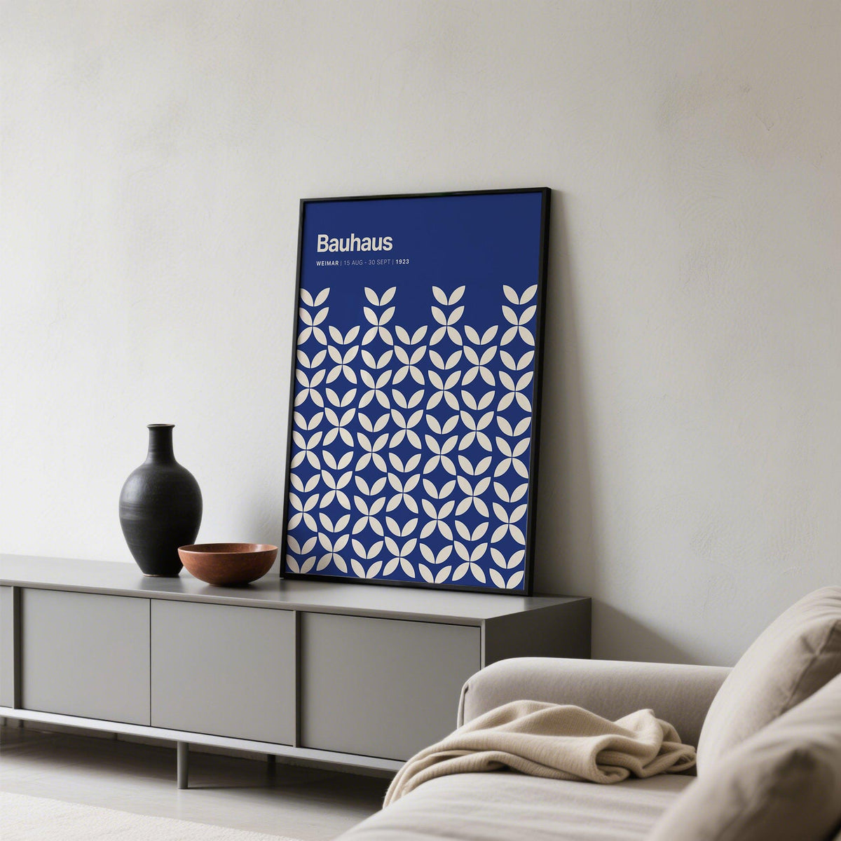 Print leaning on a shelf featuring white petal shapes on a blue background with a black frame and vases nearby
