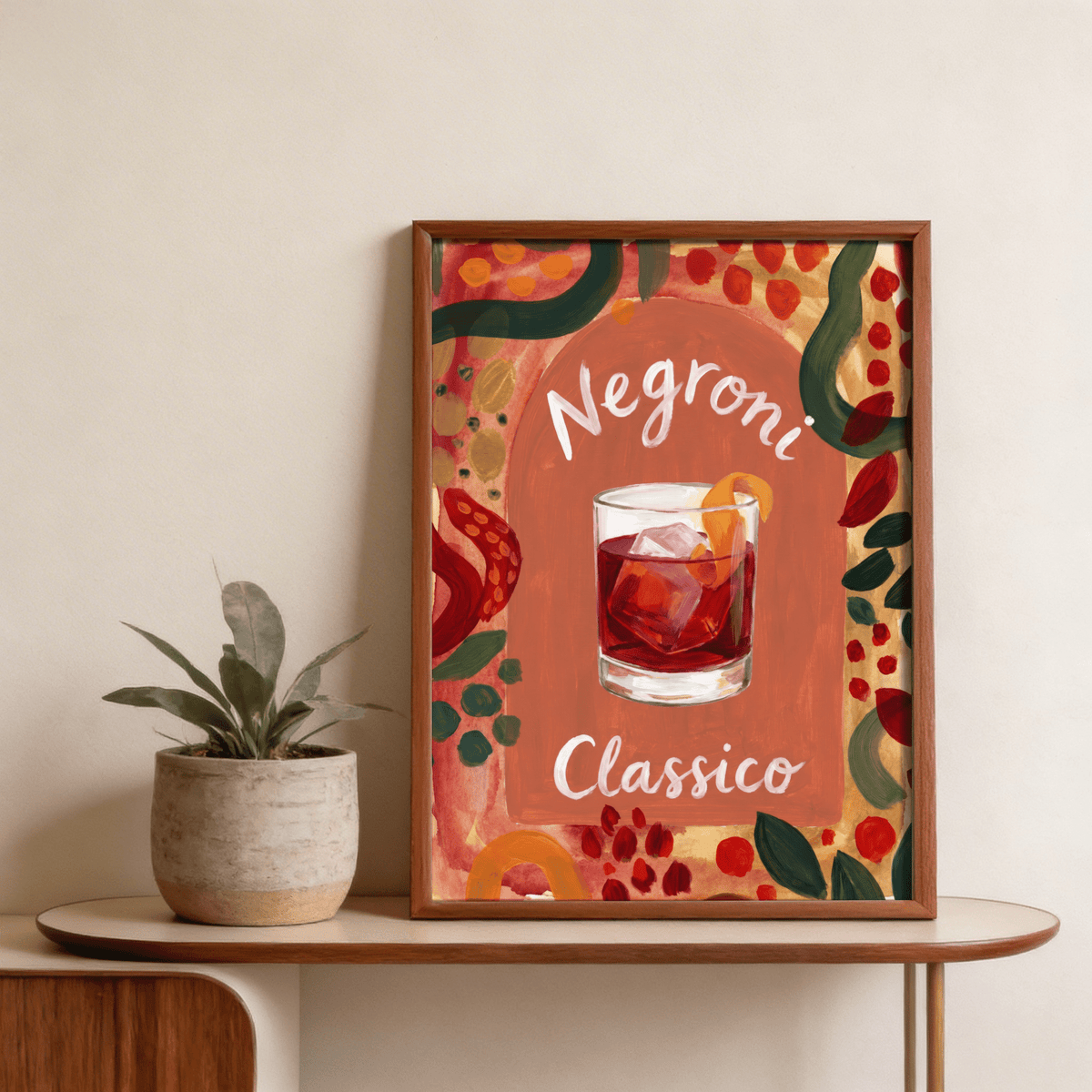 Framed Negroni Art Print of a watery negroni cocktail with a twist by a plant on a wooden table