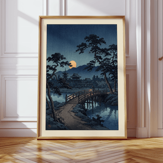 Framed Moonlit Bridge art print leaning on a wooden floor with light shadows