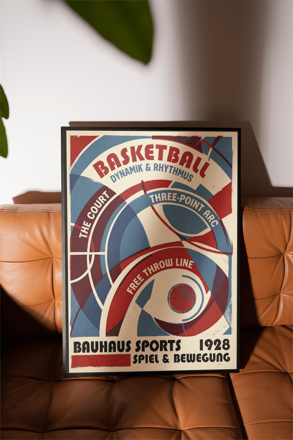 Framed Bauhaus basketball art print in blue and red leaning on a brown leather sofa with plant leaves