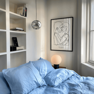 Framed Abstract Figures print of an embracing couple in black line-art above a bedside lamp with blue bedding