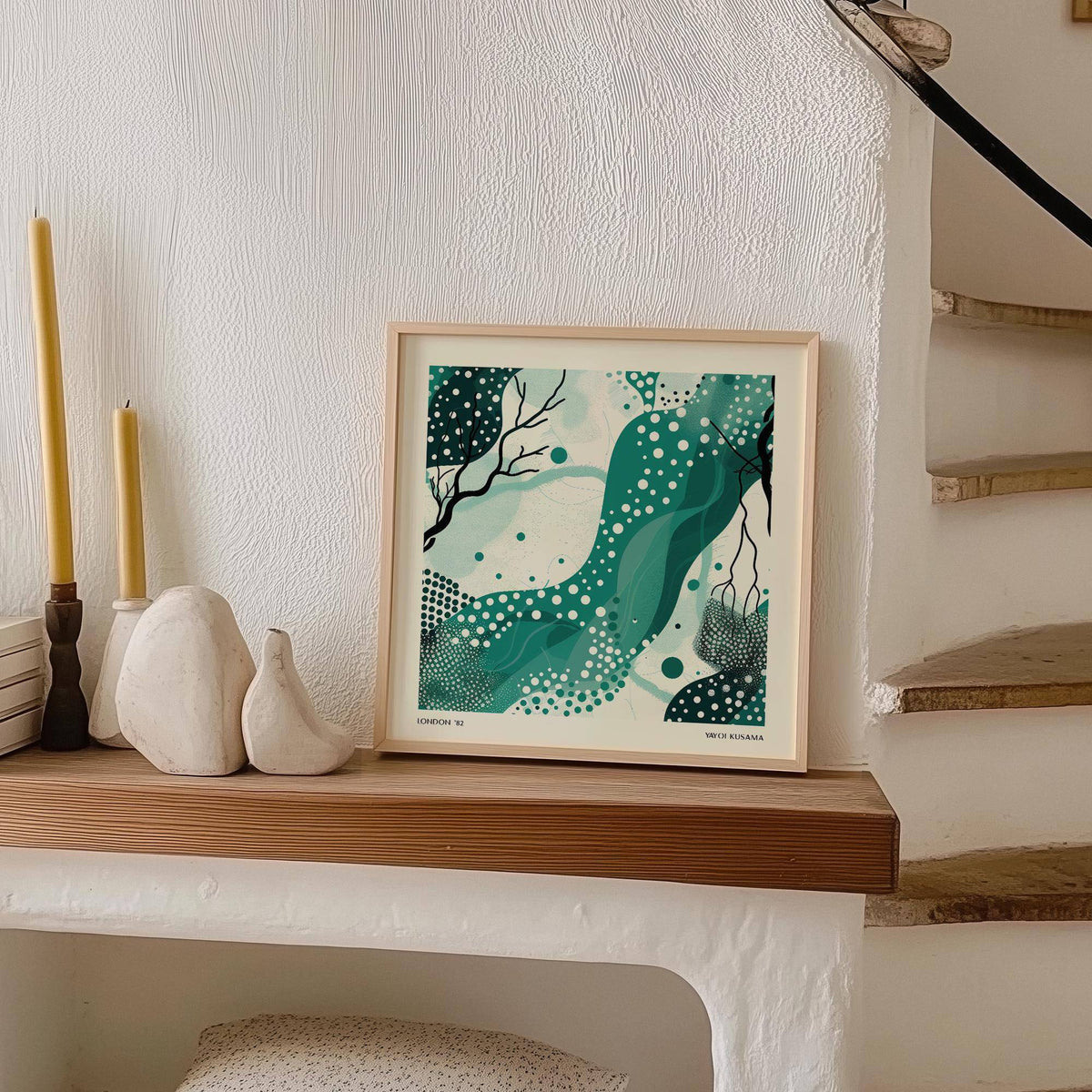 Nature wall art with abstract green shapes and white dots leaning on a wooden shelf near candles