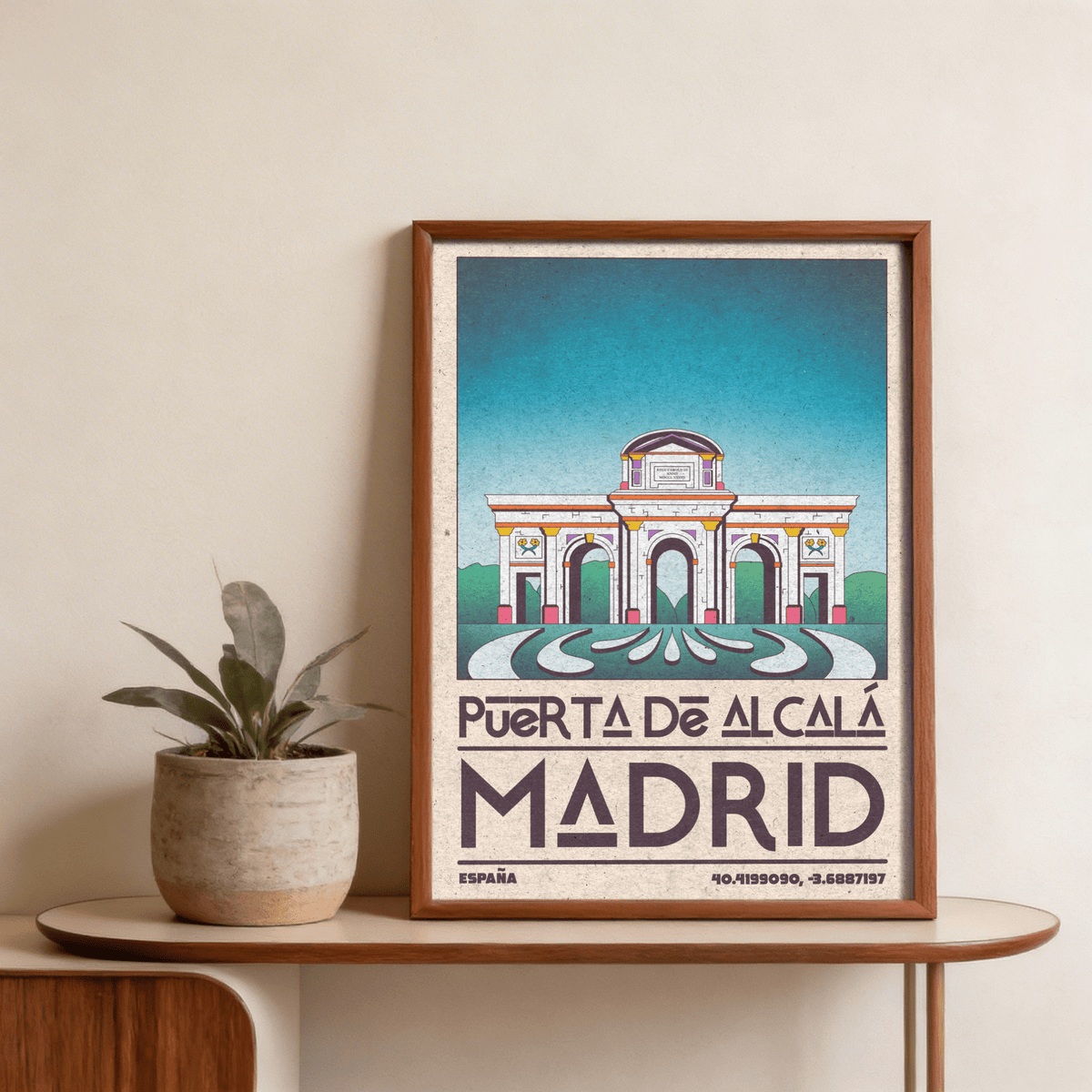 Framed Madrid Architecture Poster of the Alcalá Gateway with blue sky leaning on a wooden table beside a potted plant