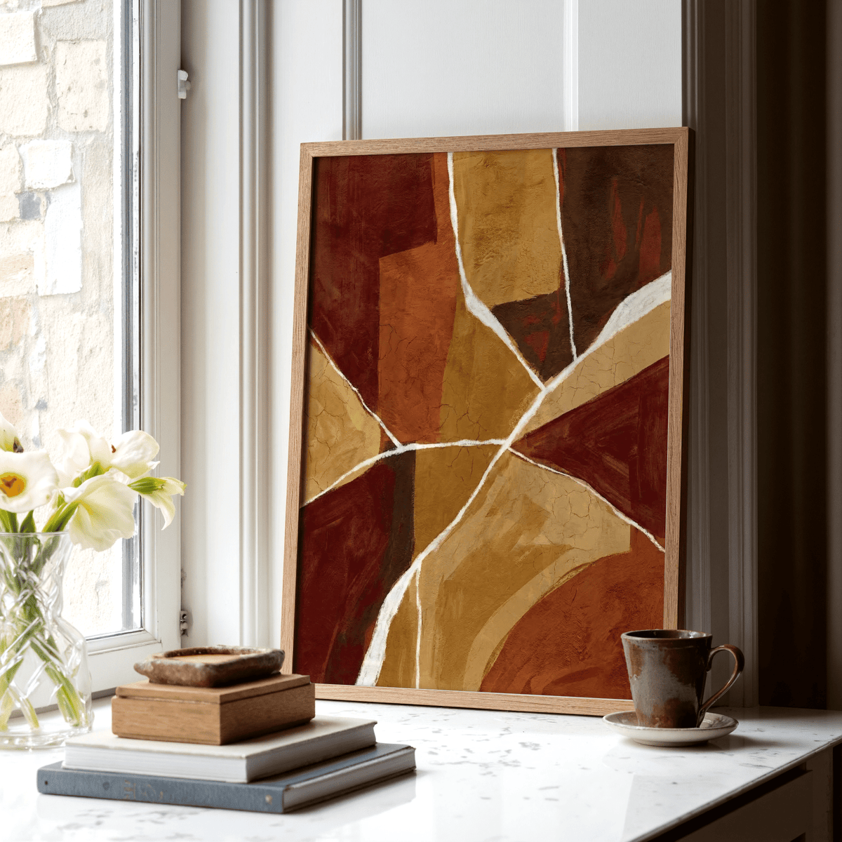 Print leaning on a shelf with burnt orange abstract art and stacked books beside it