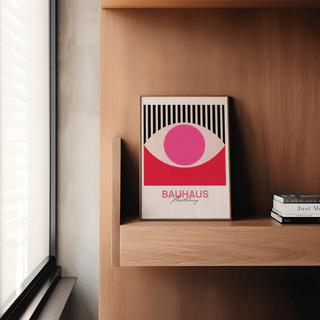 Print leaning on a wooden shelf showing abstract eye art with pink, red and black colours with stacked books nearby