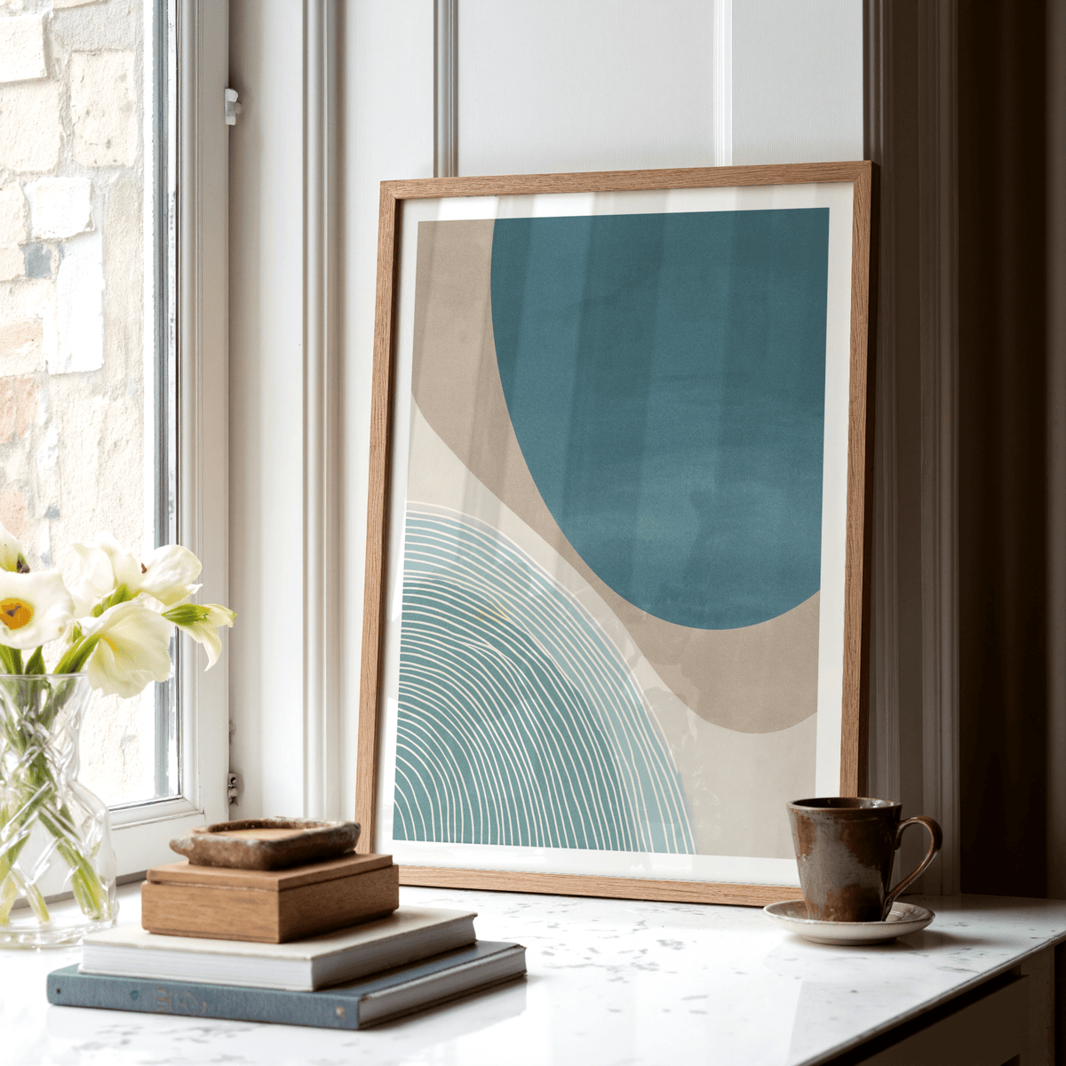 Modern Minimalist Print leaning on a window sill with books and a ceramic cup nearby in natural light