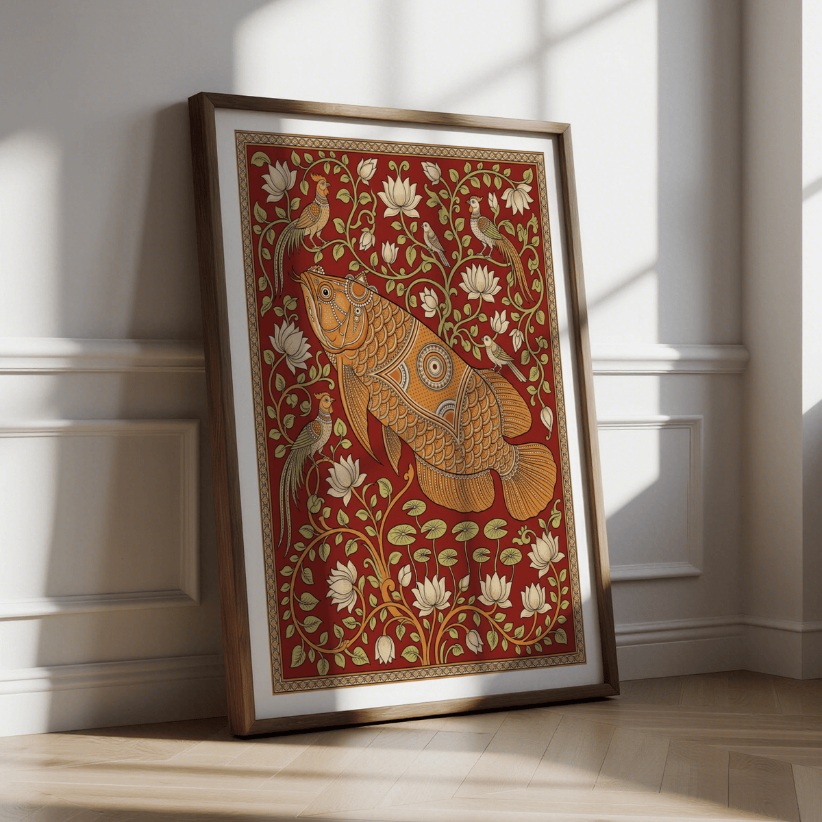 Framed Traditional Indian wall art of an orange decorative fish and birds on a red background leaning against a wall