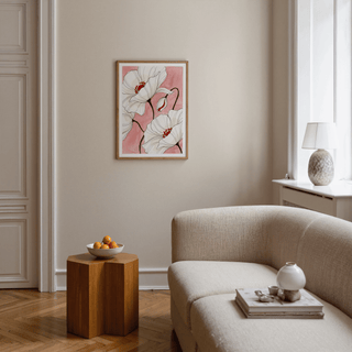 Botanical floral art print of white poppy flowers with red centres and a pink background in a living room above a wooden side table