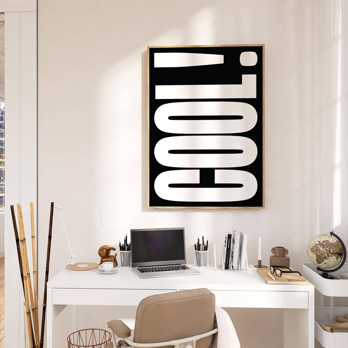 Print on a wall of 'COOL!' word in white on black above a white desk with laptop and globe