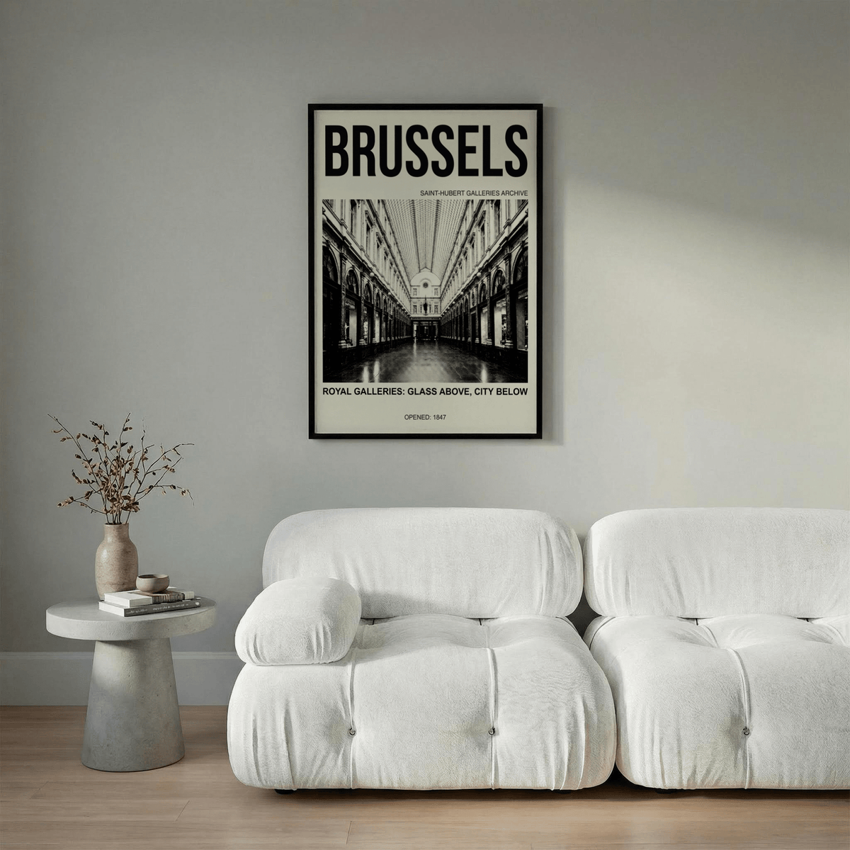 Brussels Gallery Print on a wall above white sofas and beside a table with a vase and dried plant