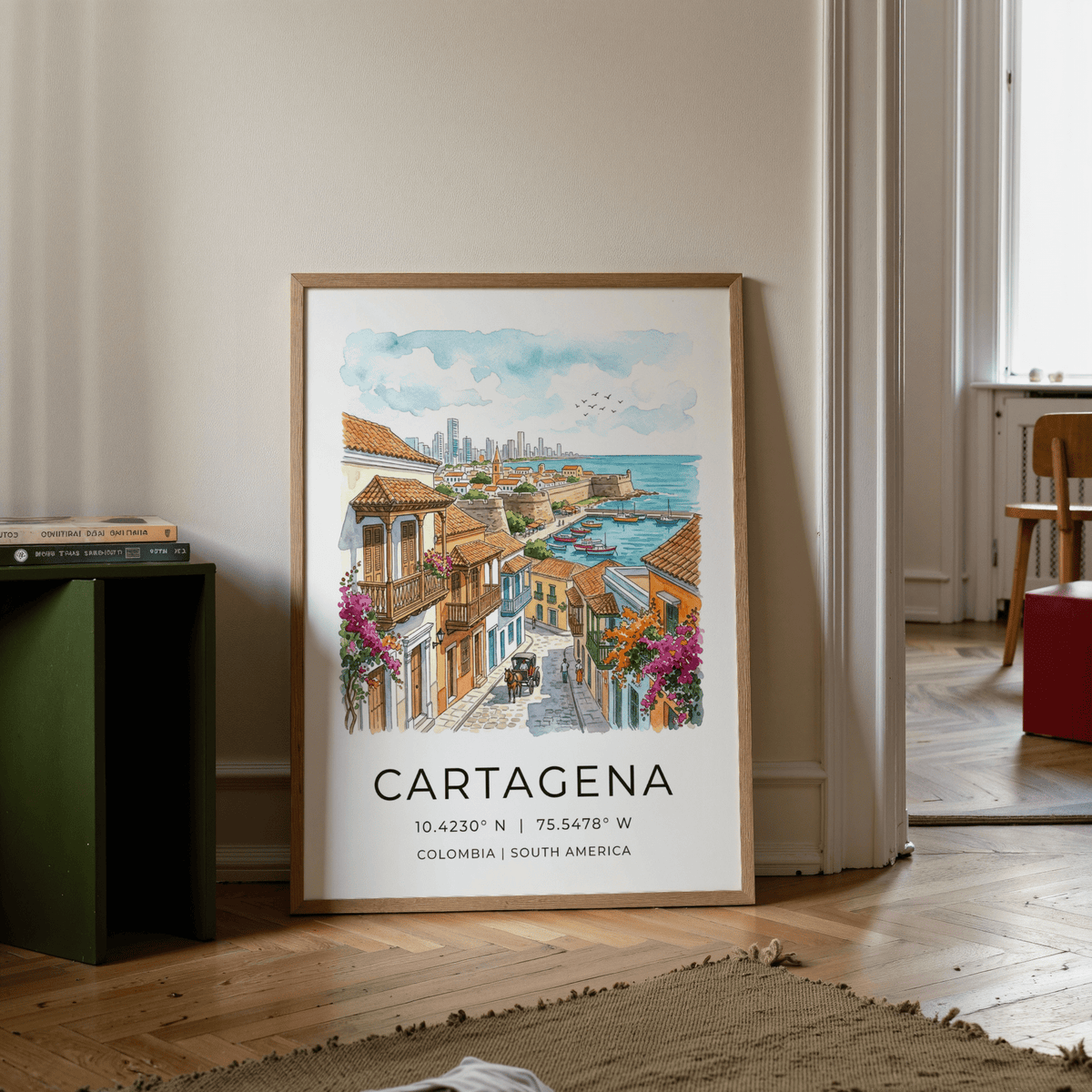 Cartagena art print leaning on a floor by a stack of books and a chair in a room