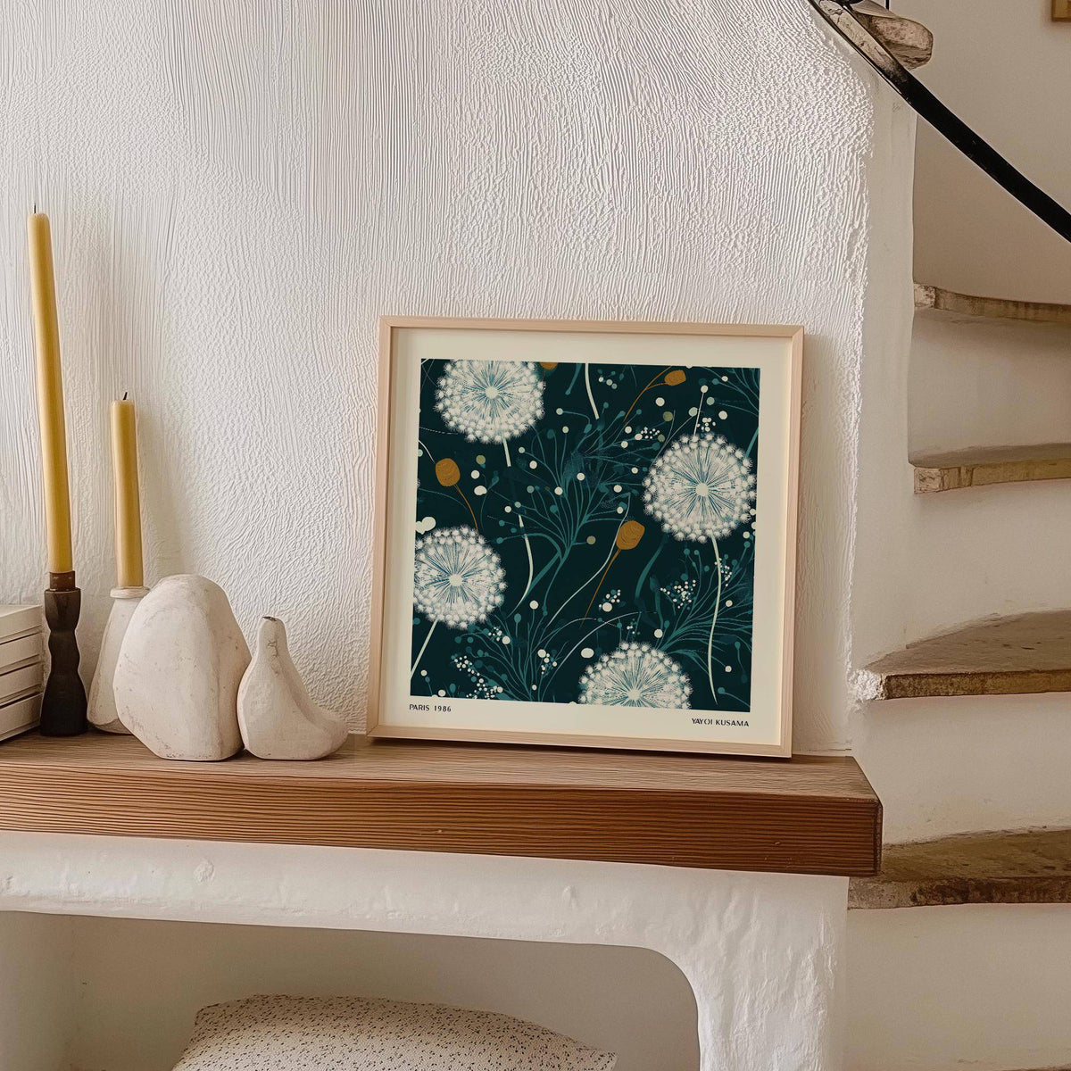 Print of dandelion wall art with white seed heads on dark background leaning on wooden mantel beside candles