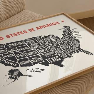 Framed close-up of US Map Poster showing typographic black states on cream background on a beige chair