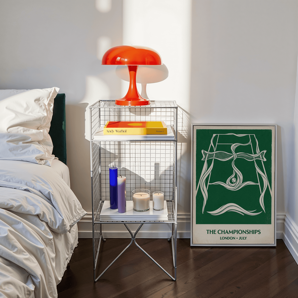 Print leaning on floor beside bedside table with red lamp and candles in a bedroom