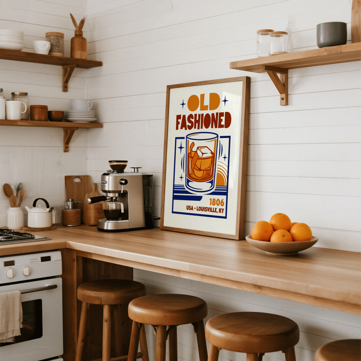 Old Fashioned Art Print leaning on a kitchen counter with wooden stools and a bowl of oranges