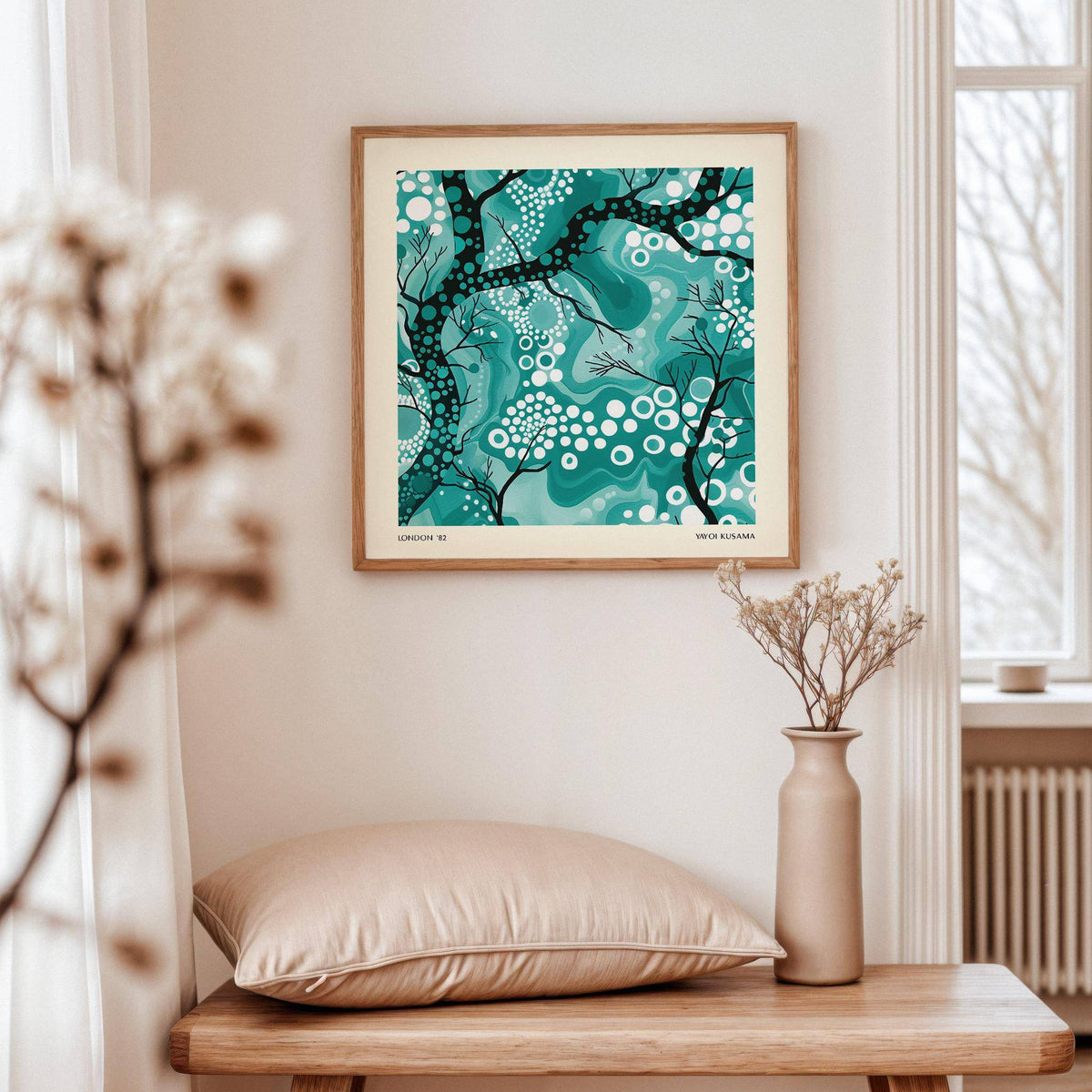 Teal abstract wall art with black tree branches and white circles above a wooden table with a beige cushion and vase