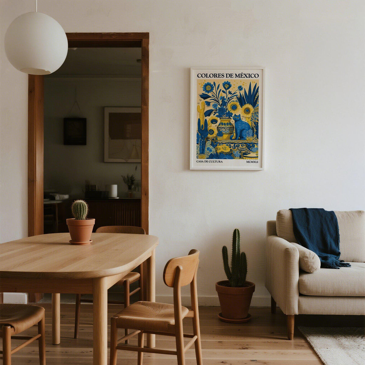 Otomi wall art of a blue cat with yellow sunflowers hanging above a wooden dining table with a cactus