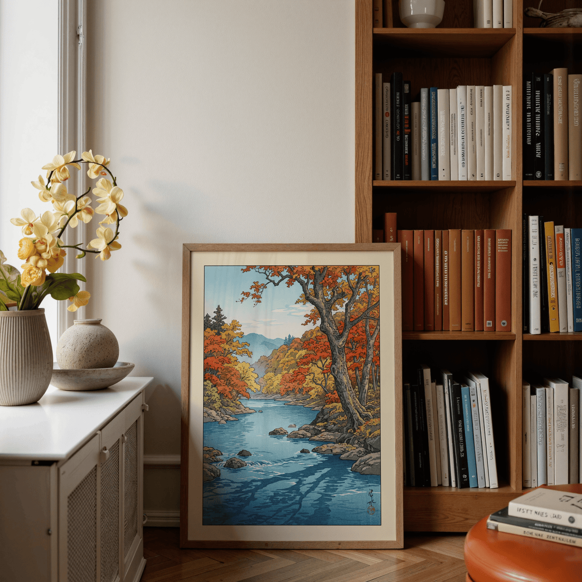 Print leaning on a shelf of a river valley with autumn trees in red and yellow next to a yellow orchid