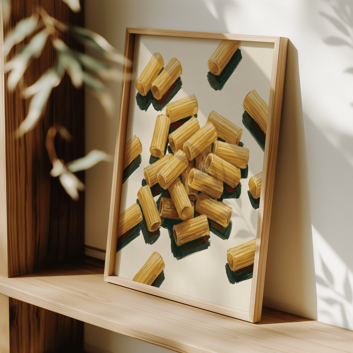 Print leaning on a shelf showing rigatoni pasta illustration in yellow and green with natural light and a leafy plant