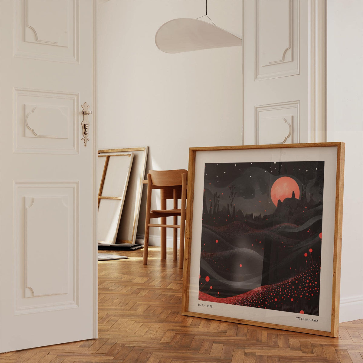 Print leaning on a floor showing a red moon landscape with dark hills and red dots a wooden chair nearby