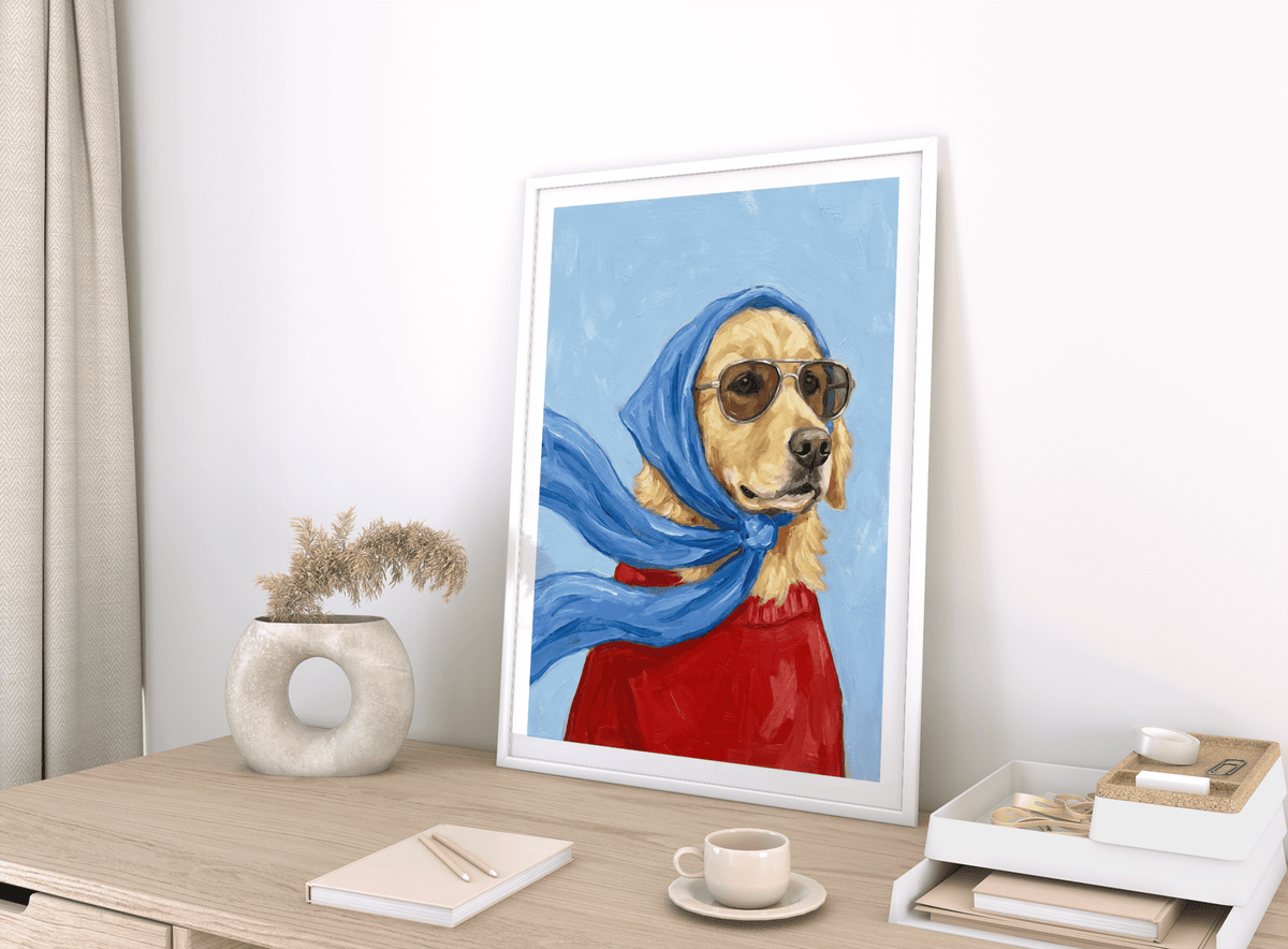 Framed Golden Retriever Art print with a blue scarf and red jumper on a light wood table with a beige vase