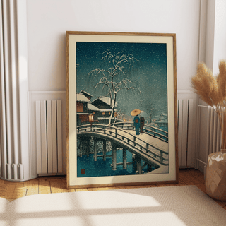 Print leaning on a floor showing snowy bridge with two people in traditional dress and a snow-filled sky