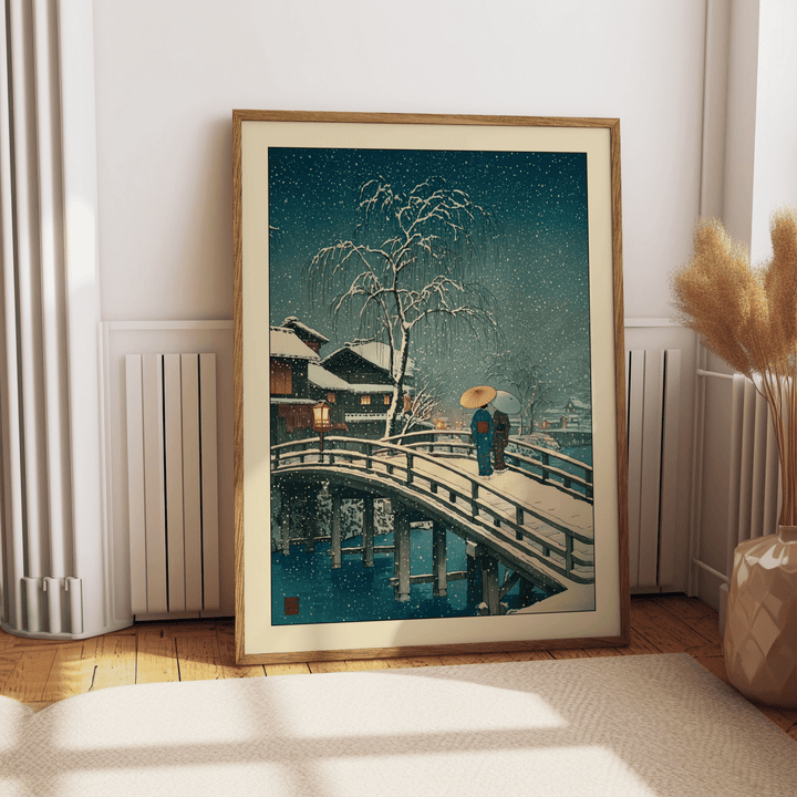 Print leaning on a floor showing snowy bridge with two people in traditional dress and a snow-filled sky